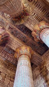 Imposing columns of the ancient esna temple featuring colorful hieroglyphic decorations on the walls and ceiling. Historical monument