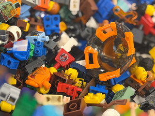 Fototapeta premium Close-up of a colorful pile of toy building bricks and minifigure parts, with an orange helmet piece among scattered plastic pieces