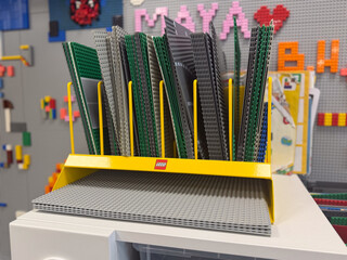 Fototapeta premium Colorful lego building plates stacked in a store display rack with a bright yellow holder and a blurred toy wall in the background.