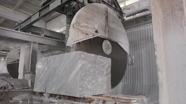 Industrial circular saw machine cutting a large marble block with water cooling in a stone processing factory