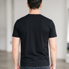 Fototapeta premium Rear view of a young adult Caucasian man wearing a plain black t-shirt standing indoors in a minimalist room with a neutral mood