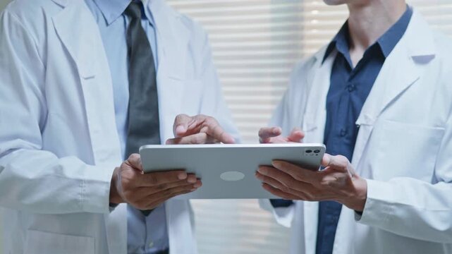 Doctors discussing a medical case together in a modern clinic office, using a tablet and laptop for telehealth, healthcare technology, medical consultation and health insurance planning.