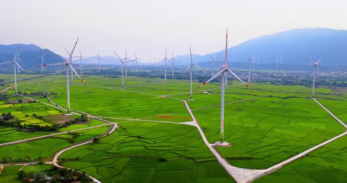 Beautiful sunrise over the Ninh Thuan wind farm, Vietnam. Golden morning sunlight illuminates vibrant green rice fields and modern wind turbines