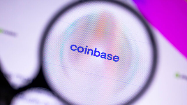 Close up view of the coinbase logo on a computer screen as seen through a magnifying glass.
