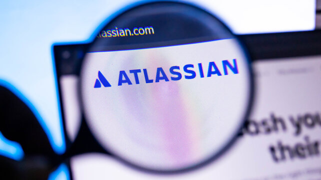 Magnifying glass showing atlassian.com homepage on a laptop screen with company's logo and website address.