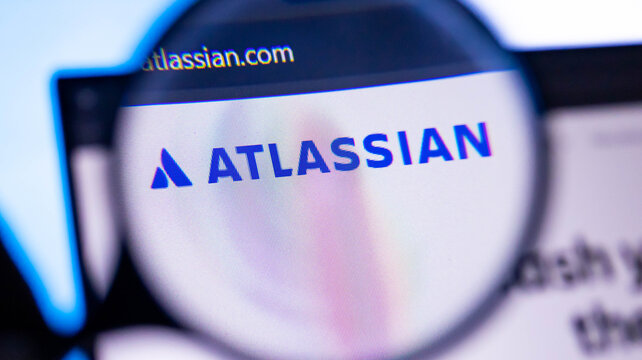 Magnifying glass focusing on atlassian.com homepage on a laptop screen with company's logo and website address.