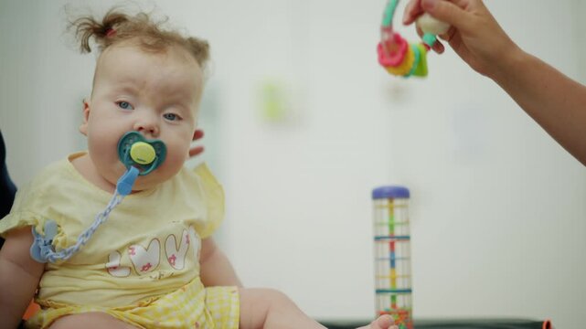 Baby with pacifier engaging in a physical therapy session for developmental assessment, supported by a blurred professional