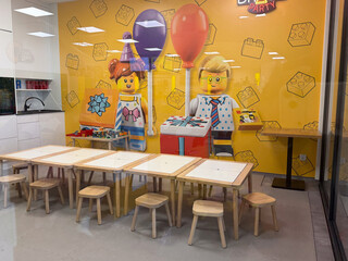 Fototapeta premium Bright lego-themed birthday party room with small tables, stools, balloons, and cartoon brick characters on a yellow wall indoors.