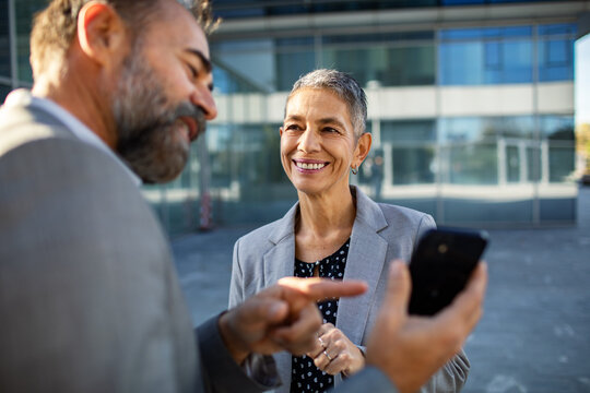 Smiling business colleagues reviewing smartphone outside office