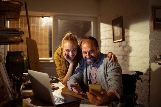 Smiling couple using laptop and smartphone in home office at night