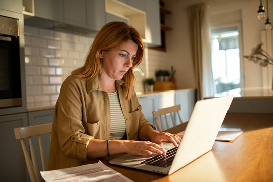 Focused woman working on laptop at kitchen table at home