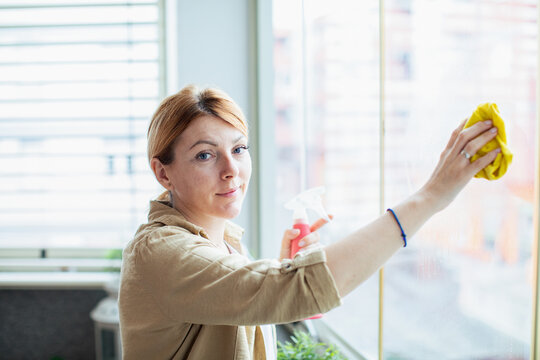 Woman cleaning apartment window with spray bottle at home