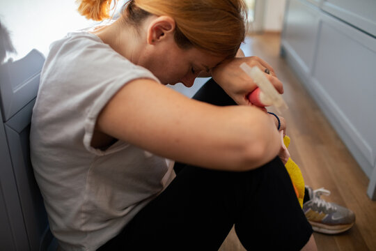 Stressed young woman sitting on kitchen floor after cleaning