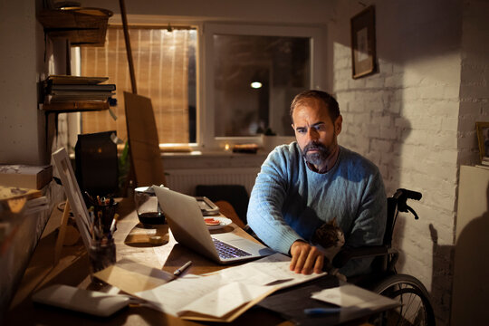 Man in wheelchair working late on laptop at home office