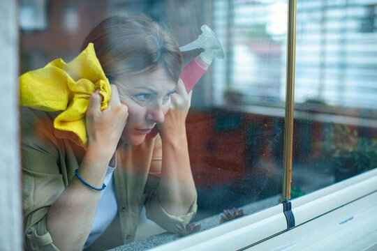 Frustrated woman cleaning window at home