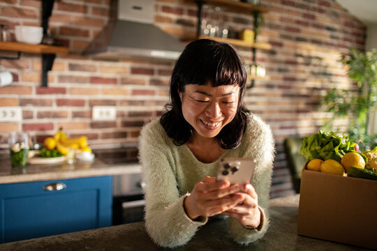 Smiling woman using smartphone in cozy home kitchen