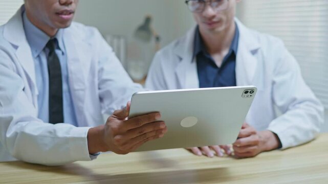 Doctors discussing a medical case together in a modern clinic office, using a tablet and laptop for telehealth, healthcare technology, medical consultation and health insurance planning.