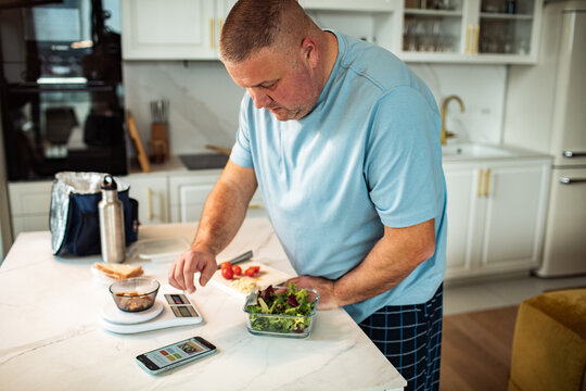 Middle-aged man meal prepping with food scale in home kitchen