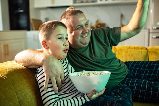 Father and son watching tv with popcorn at home