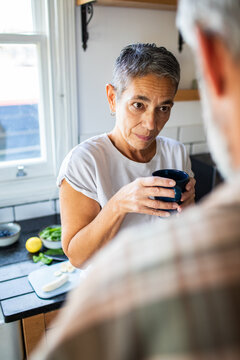 Mature woman holding coffee mug during serious conversation at home kitchen