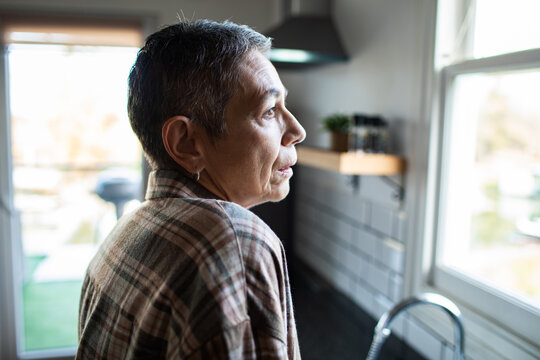 Thoughtful older adult looking out kitchen window at home