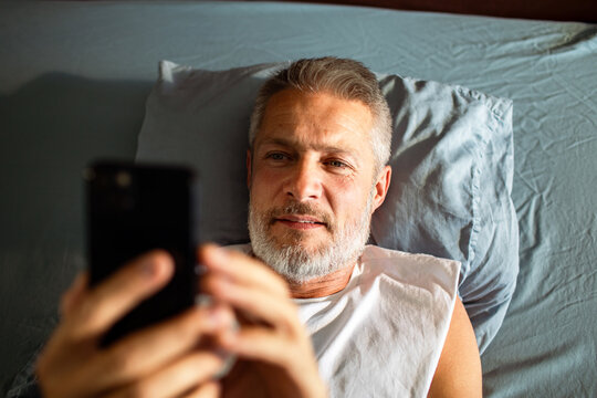 Mature man using smartphone in bed at home