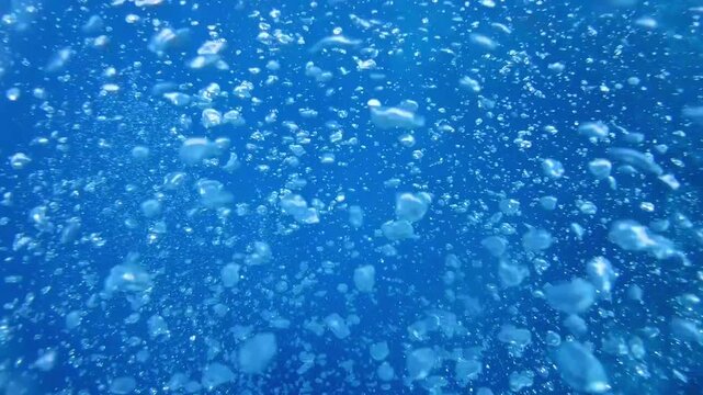 Underwater scene showing bubbles rising through clear blue ocean water, capturing the dynamic flow and movement of air as it ascends towards the surface