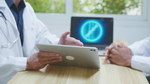 Doctors consulting together in a modern medical office, reviewing information on a tablet and computer for medical research, telehealth planning, healthcare technology, and collaborative clinical disc