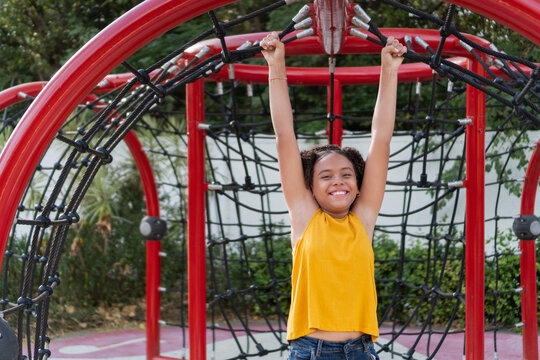 Smiling teen girl hanging on playground climbing structure