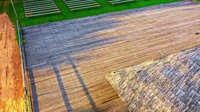 Empty outdoor venue with a wooden stage and benches on green grass waiting for a performance