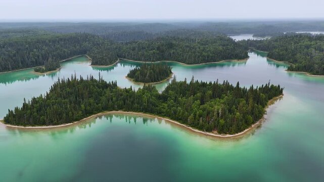 Aerial view of a picturesque forested island surrounded by vibrant turquoise and blue-green waters on Arnott Lake in northern Ontario, bordered by pristine boreal forest.