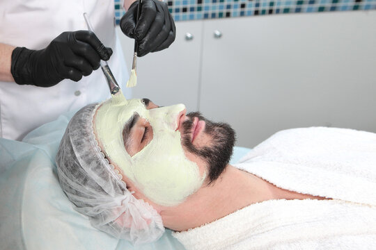 Cosmetologist applies a mask to a man's face at a spa. Facial treatments at a beauty salon. Men's cosmetology. Natural clay mask. Natural cosmetics