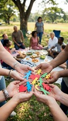 Fototapeta premium Diverse group of adults and children holding colorful paper cutout figures in circle formation during outdoor park gathering, symbolizing community unity and togetherness for nonprofit campaigns.