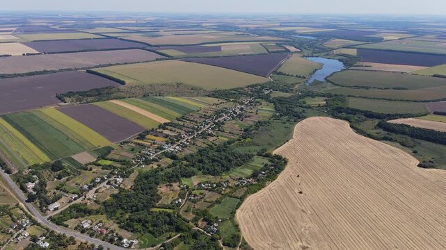 Smooth aerial flight over Talianky village in Ukraine, revealing rural houses, green gardens, several ponds, and agricultural fields surrounding the settlement in summer.