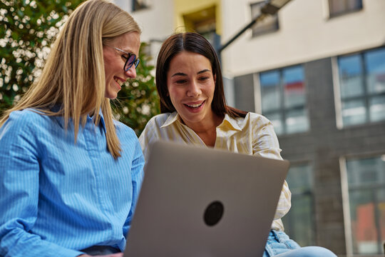 Women colleagues discussing business project using laptop outdoors