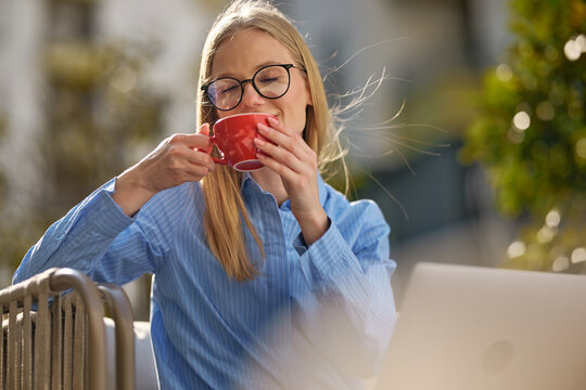 Young woman enjoying coffee working outdoors with laptop