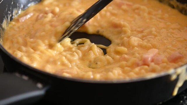 Homemade mac and cheese being stirred in a skillet