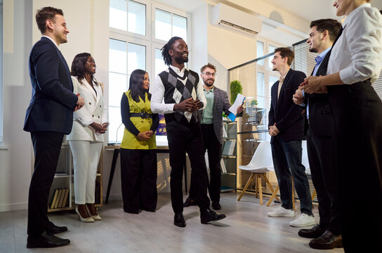 Team employees meet colleagues for office recognition. A coworker speaks as the leader and group offer applause, guiding the meeting forward. Clear concept of teamwork and open discussion.