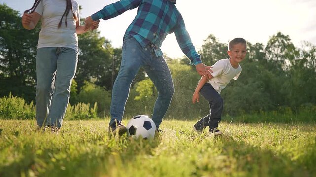 The father stands between the boy and girl, guarding the football. The children laugh while playing. This joyful game between the man and his children shows how much they love playing soccer together.