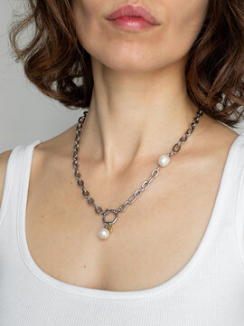 Stylish woman in white top wearing pearl and steel chain - modern minimalist jewelry fashion portrait in natural light