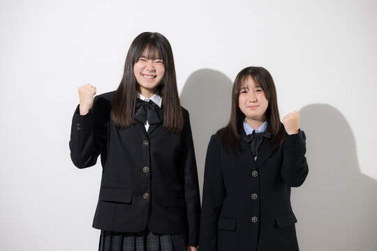 白背景で未来や将来へ向かってがんばるガッツポーズカメラ目線上半身　日本人女子高生や中学生　2人で前向きに進む受験や青春、合格やオープンキャンパスイメージ