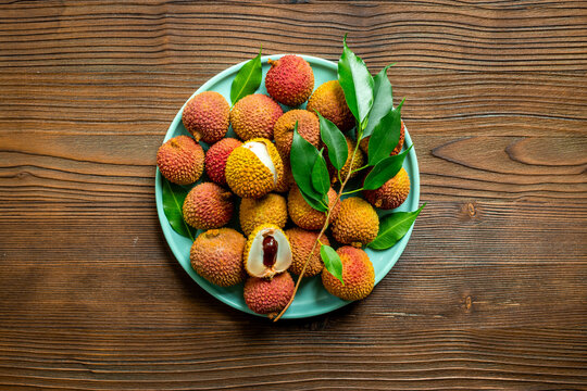 Fresh lychee fruit with green leaves on a plate, top view
