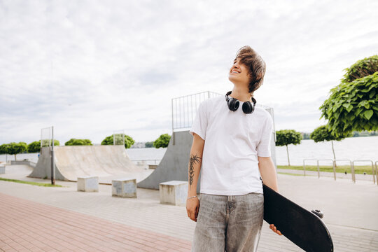 Teenager holding skateboard smiling looking up at skatepark