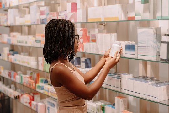 Woman choosing skincare product from shelf in beauty store reading label before purchase