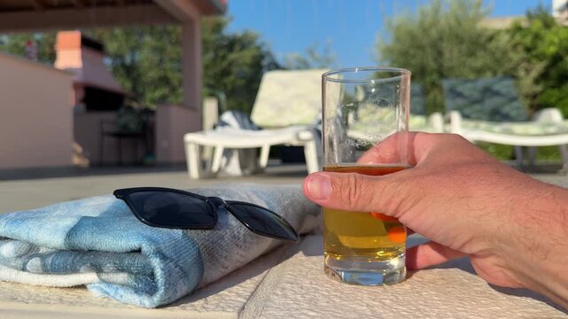 A chilled glass of beer rests beside a swimming pool at an exclusive apartment in Croatia. A sun lounger with a towel and sunglasses creates a relaxing summer atmosphere, perfect for enjoying a refres