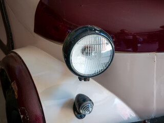 A detailed close-up shot captures the round glass headlight and signal lamp of a classic vintage vehicle with white and maroon bodywork. © Dmitry