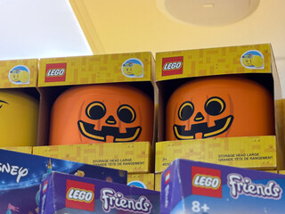 Fototapeta premium Boxed lego pumpkin storage heads with jack-o'-lantern faces displayed on a store shelf, with other toy boxes in the foreground