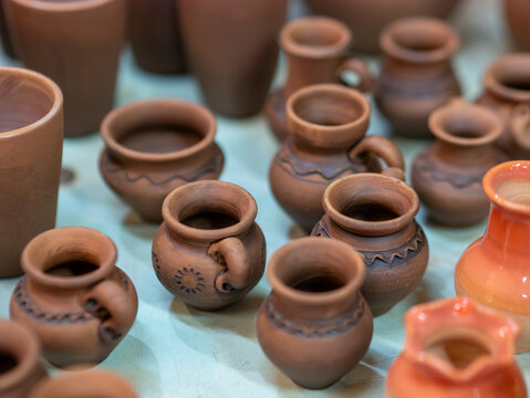A high-angle close-up shot shows a collection of traditional terracotta and glazed clay pots arranged on a workbench in a pottery studio.