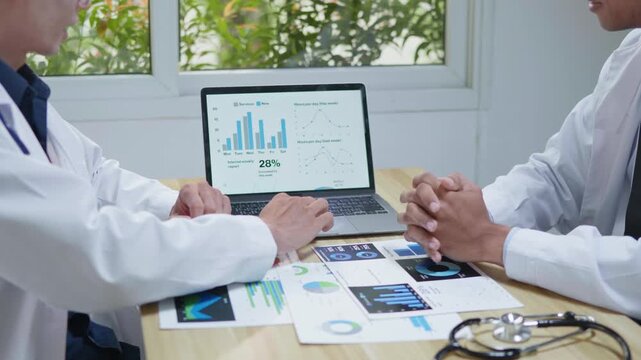 Doctors consulting together and planning treatment in a modern medical office, reviewing healthcare data, charts, and reports on a laptop for clinical decision making and patient care.