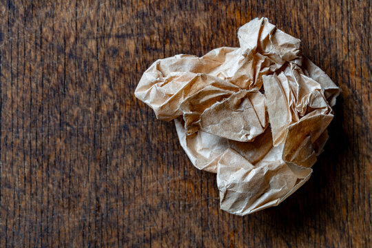 Crumpled brown paper ball on dark wooden table with copy space, closeup. Textured recycled paper trash symbolizing mistake or brainstorming process. Ideal for business and eco concepts